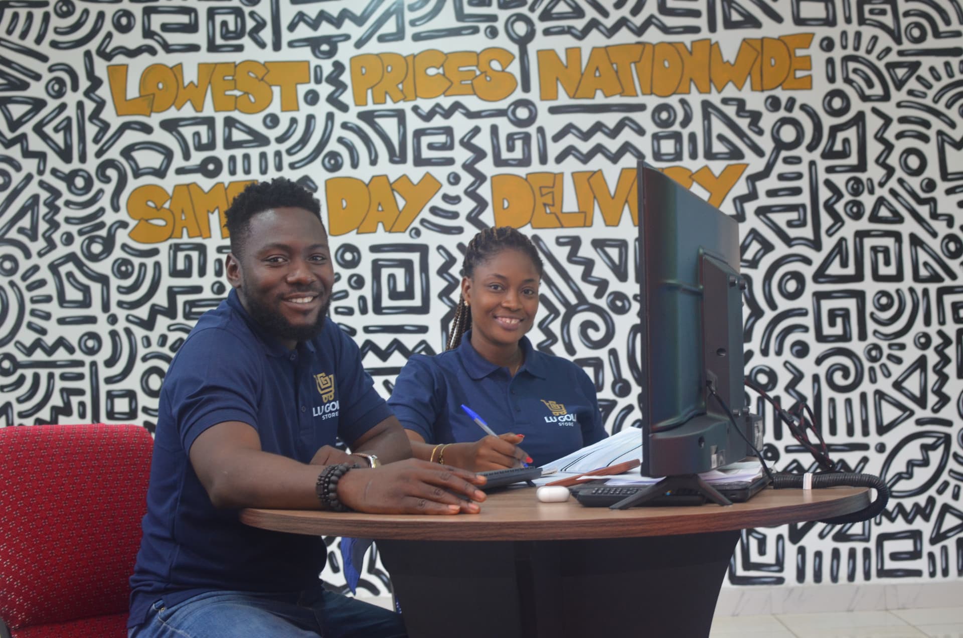 Lu Gold Store staff at the Abuja showroom desk in front of a Lowest Prices Nationwide mural